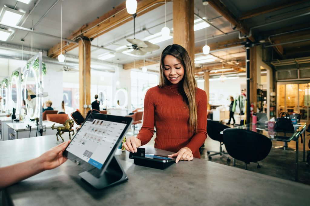 A woman in a red sweater using a credit card to pay for a cup of coffee.